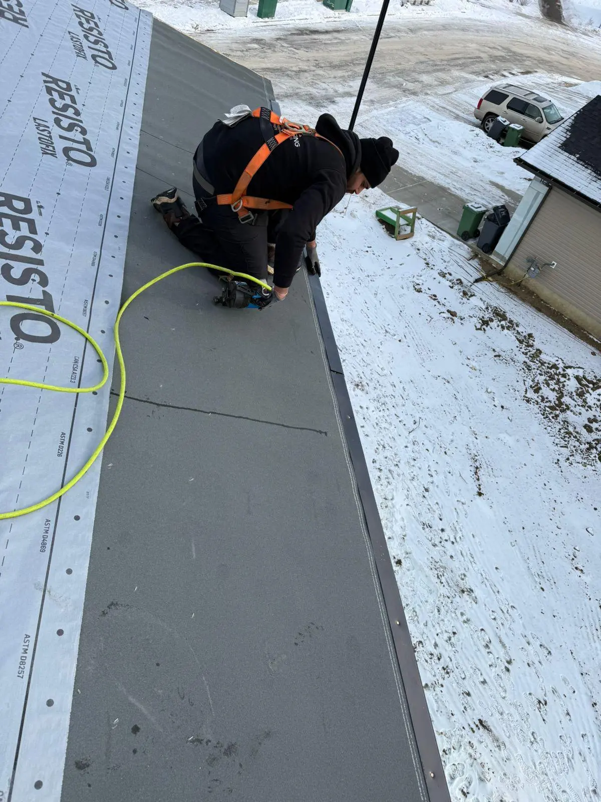 Roofer securing membrane along a roof edge during a winter install